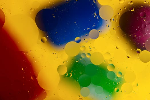 Abstract oil spots in motion on water on blurred yellow background. Red, green, purplee and blue spots on blurred background. Photo with small depth of field.