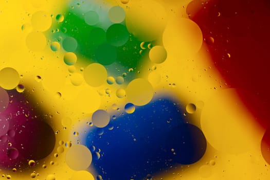 Abstract oil spots in motion on water on blurred yellow background. Red, green, purplee and blue spots on blurred background. Photo with small depth of field.