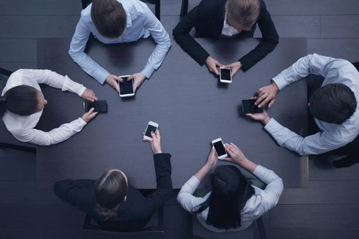 Business people with smartphones sitting around the table, top view