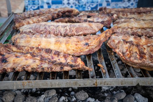 BBQ rack of pork ribs lined up on a large outdoor grill with smoke coming up from the fire below.