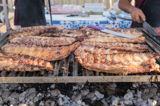 BBQ rack of pork ribs lined up on a large outdoor grill with smoke coming up from the fire below.