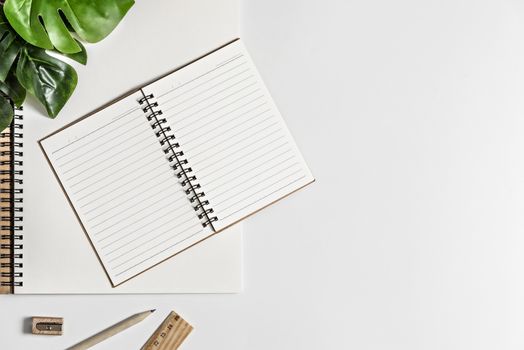 Flat lay of white office desk table with blank notebook, supplies and coffee cup. Top view with copy space.