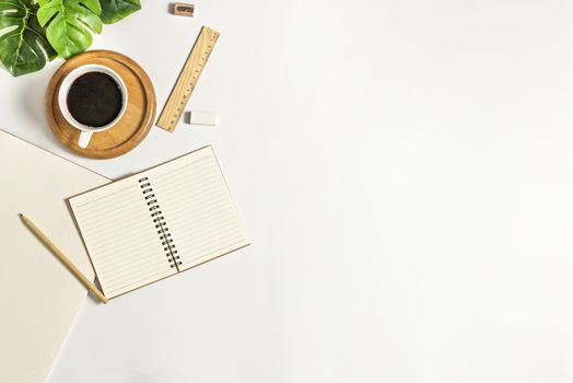 Flat lay of white office desk table with blank notebook, supplies and coffee cup. Top view with copy space.