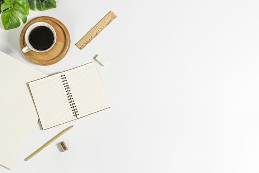 Flat lay of white office desk table with blank notebook, supplies and coffee cup. Top view with copy space.