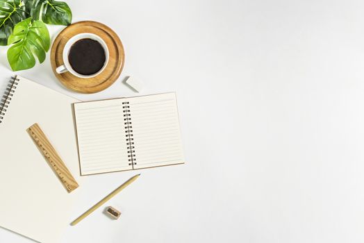 Flat lay of white office desk table with blank notebook, supplies and coffee cup. Top view with copy space.