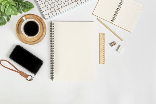 Flat lay of white office desk table with blank notebook, supplies and coffee cup. Top view with copy space.