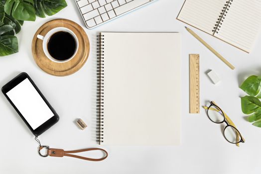 Flat lay of white office desk table with blank notebook, supplies and coffee cup. Top view with copy space.