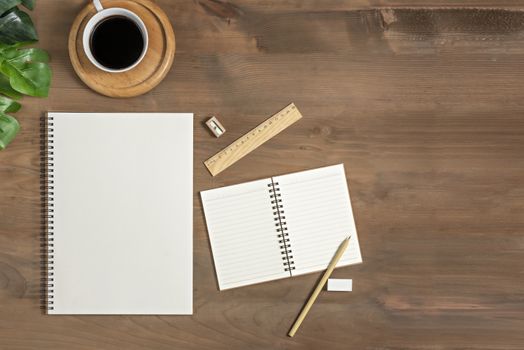 Flat lay of wooden office desk table with blank notebook, supplies and coffee cup. Top view with copy space.