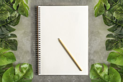 Top view and flat lay with blank sketchbook and green leaves over cement background