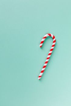 Christmas peppermint candy cane on pastel turquoise background. Festive minimal style flat lay. Mockup with copy space for greeting card, invitation, social media. Vertical.