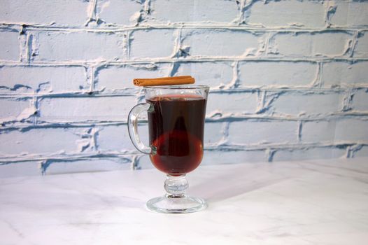 A glass cup of hot mulled wine with a slice of orange and a cinnamon stick. Close-up.