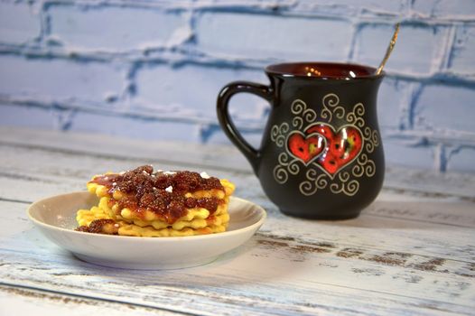 Black ceramic cup with tea m saucer with waffles and strawberry jam. Close-up.