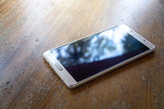 The smart phone is on a wooden table on a bright sunny day.