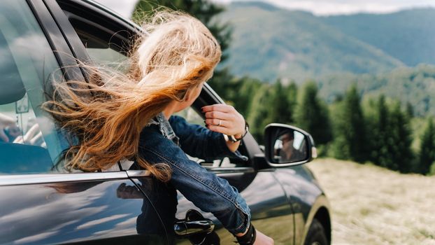 Happy woman travels by car in the mountains. Summer vacation concept. Woman out the window enjoying mountain view