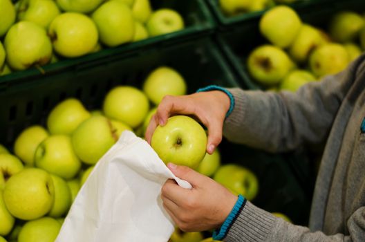 Children's hands put apples in a bag of cotton at the supermarket. Reusable environmental shopping bag. Zero waste concept - reuse.