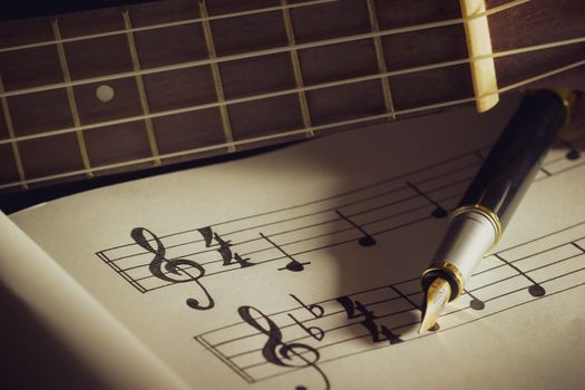 Music notes and ukulele in morning light. Writing chords by vintage pen. Closeup and copy space for text. Concept of Music lovers.