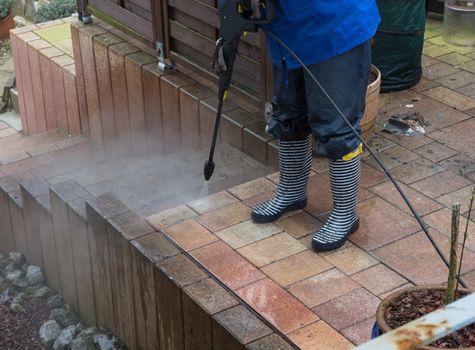 Woman cleans stone slabs with a pressure washer