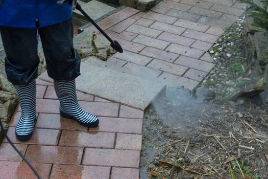 Woman cleans stone slabs with a pressure washer