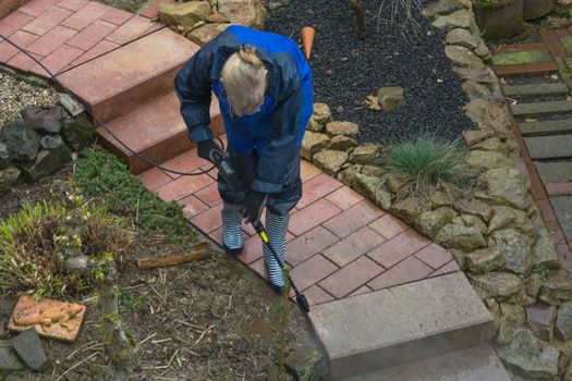 Woman cleans stone slabs with a pressure washer