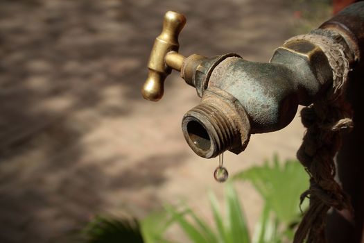 Image of a drop of water falling from an old metal conduct. The last drop of water