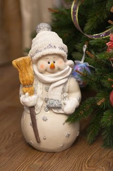 Funny happy snowman with broom by the christmas tree in evening time. Homemade festive cozy atmosphere. Front view. Vertical.