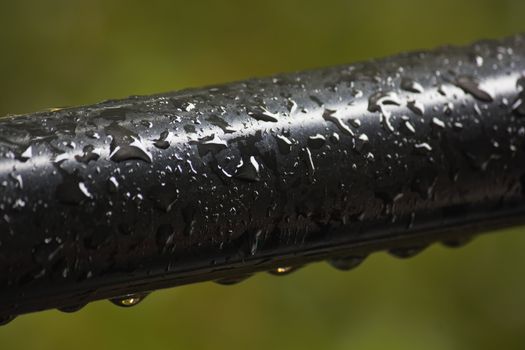 Smooth black wet handrail bar covered in rainwater droplets during summer rain thunder showers