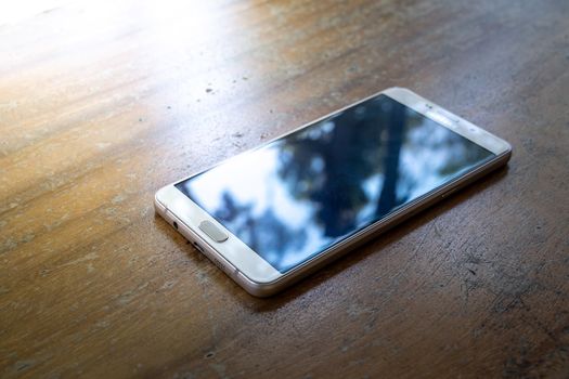 The smart phone is on a wooden table on a bright sunny day.