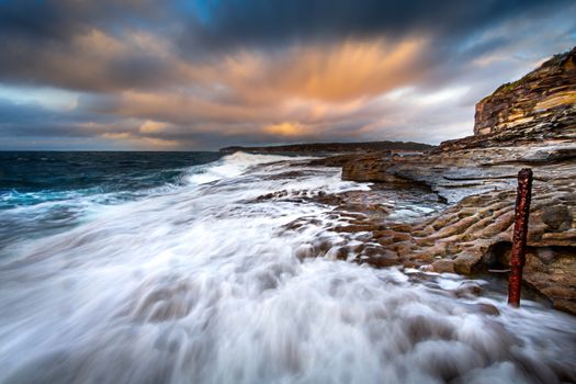 W strong wind picking up the waves and swell creating strong onshore flows around the rocks of Bare Island and creating great movement of clouds in long exposure