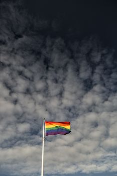 Rainbow Flag waving in the wind with a partly cloudy sky.