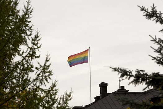 Rainbow Flag waving in the wind on Roof with a cloudy sky.