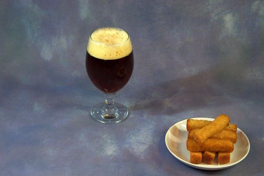 A glass of dark beer and a plate with wheat croutons. Close-up.