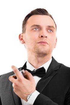 A portrait of a young handsome man in a suit using a perfume, isolated on white background.