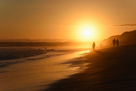 Golden beach summer vacation landscape scene at sunset with people walking, Mossel Bay, South Africa