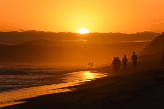 Sun setting behind the clouds causing a vibrant orange glow at last light on beach, Mossel Bay, South Africa