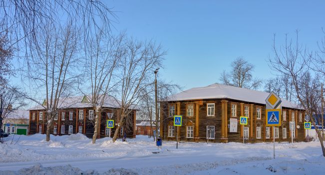 Wooden, old, two-story houses on a snowy street with pedestrian crossing road signs.