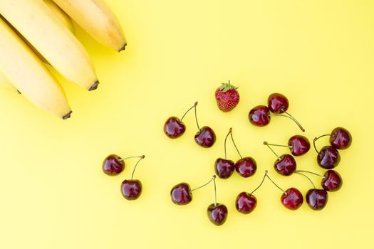 ripe fresh cherry, strawberry and bananas on a yellow background