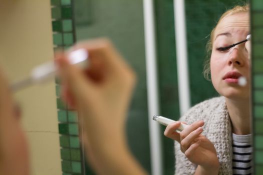 Morning routine. Casual beautyful woman applying maskara makeup in front of a mirror in the morning.