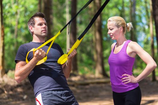 Young active people does suspension training with fitness straps outdoors in the nature.