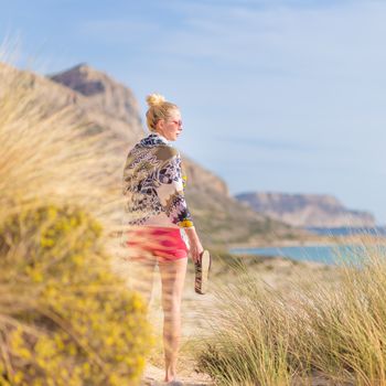 Relaxed woman wrapped in colorful scarf, enjoying sun, freedom and life at beautiful Balos beach in Greece. Concept of holidays, vacations, freedom, joy and well being.