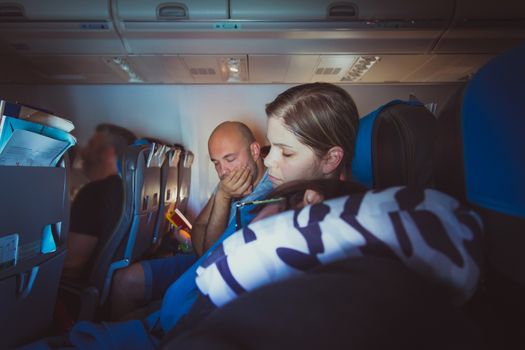 Tired caucasian men and women sleeping on seats while traveling in a commercial airplane.
