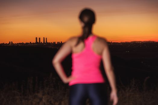 Woman on sport clothes watching sunset over city skyline. Focus is on background.