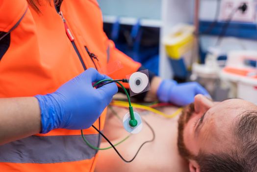 Emergency doctor hands, attaching ecg electrodes on patient chest in ambulance
