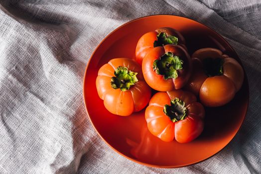 Some Persimmons on Orange Plate. High Angle View