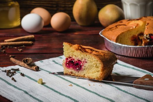 Slice of cherry cake on a striped towel, and other objects on background.