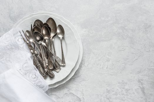 Various silverware on a porcelain plate and white napkin with Belgian lace are on the background of gray concrete surface, with copy-space