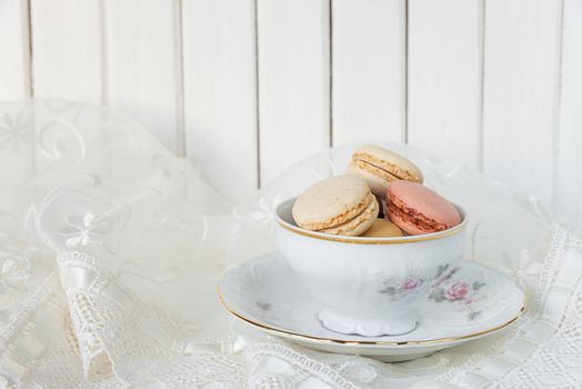 Beautiful elegant porcelain cup filled with almond cookies, on the background of white lace fabric