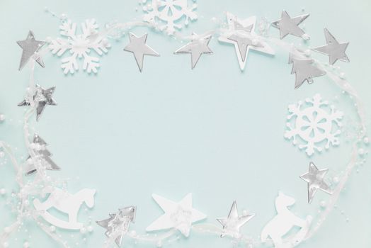 Christmas frame composed of white christmas decoration: snowflakes, stars, Christmas trees and toy; rocking horse on blue background. Flat lay composition for greeting card, websites, social media, magazines,  bloggers, artists etc.