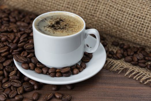 Cup of black coffee with roasted coffee beans on the dark wooden background with rough burlap