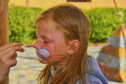 Beautiful young girl with face painted like a rabbit.  Face painting on child face.