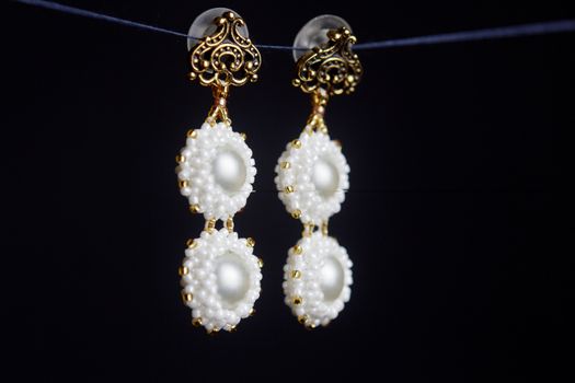 handmade jewelry made of beads in macro. earrings from white beads. earrings from stones. beautiful ornaments. earrings from white beads. ornaments on a black background